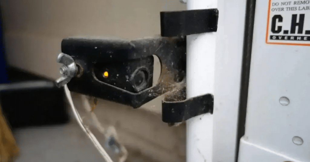 Garage door sensor with visible cobwebs and an indicator light.